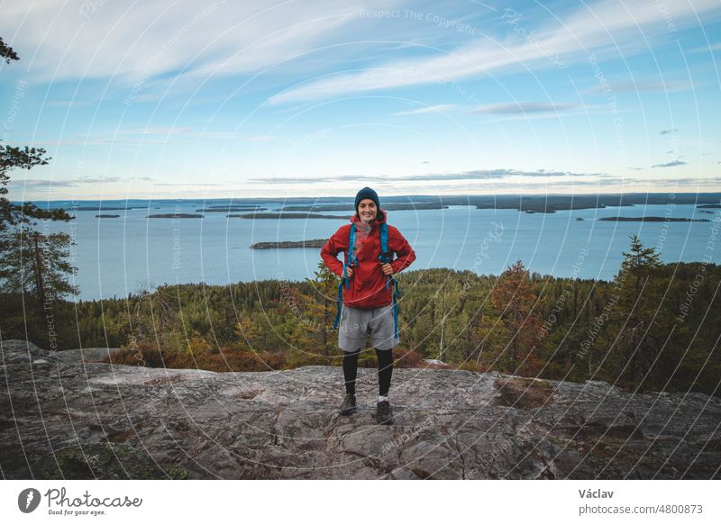 Laughing backpacker standing on a rock with Lake Jatkonjarvi behind him in Koli National Park, eastern Finland. The man, aged 24, smiles naturally. Active lifestyle