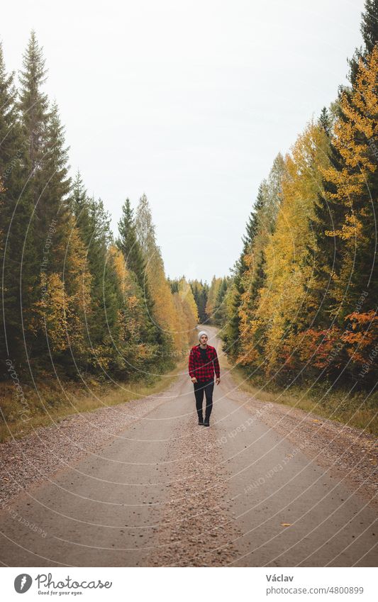 Man aged 23 wearing a checked red and black shirt walks along a foamy path surrounded by beautiful deciduous trees coloured in autumn colours. Enjoy the moment. Kainuu region, Finland