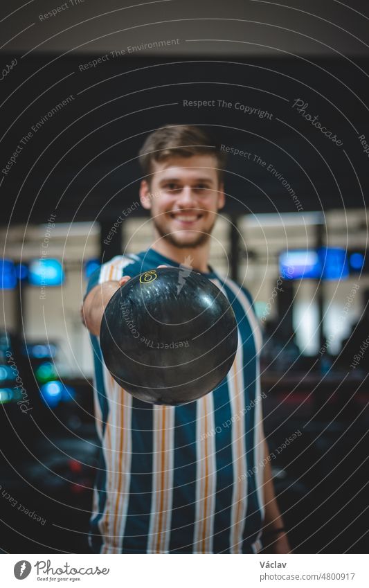 young amateur bowler wearing spotted t-shirt takes the correct ball and with real smile concetrate for another shot. Blond guy ready for starts of competition. Sotkamo, Finland