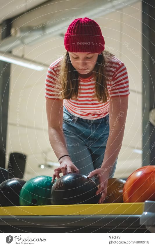young amateur female bowler wearing a red cap and a spotted t-shirt takes the correct weight ideal ball and prepares internally for her throw. Concentration
