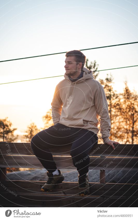 Male model in a beige sweatshirt sits on top of Vuokatinvaara mountain, in the kainuu region, Finland. a man with an athletic figure with a realistic smile enjoys the sunrise and autumn