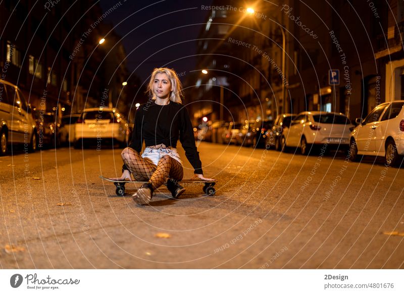 young woman in shorts on a long board while looking camera at night in the city front view sensual wall charming girl fashionable lifestyle skateboarder shadows