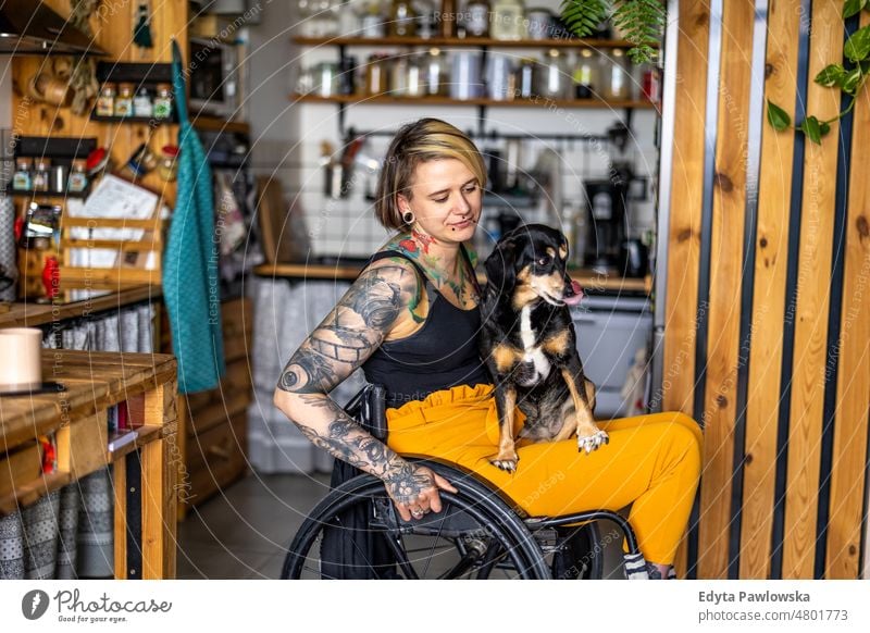 Young tattooed woman in a wheelchair with her dog at home domestic life confidence indoors house people young adult casual female Caucasian attractive beautiful