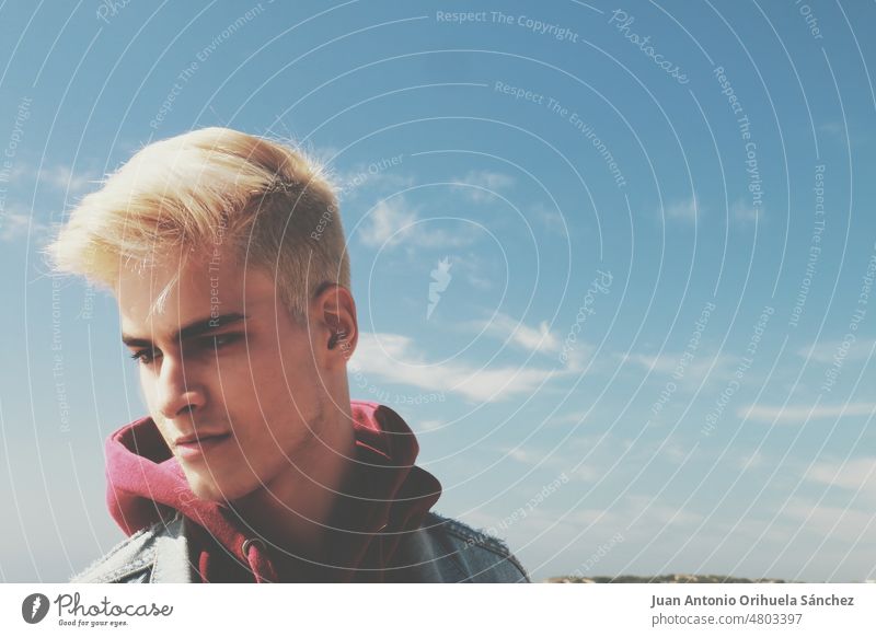 Closeup portrait of a handsome and attractive blond boy with sky background teen teenager man guy one man close-up trendy fashion fashionable bizarre natural