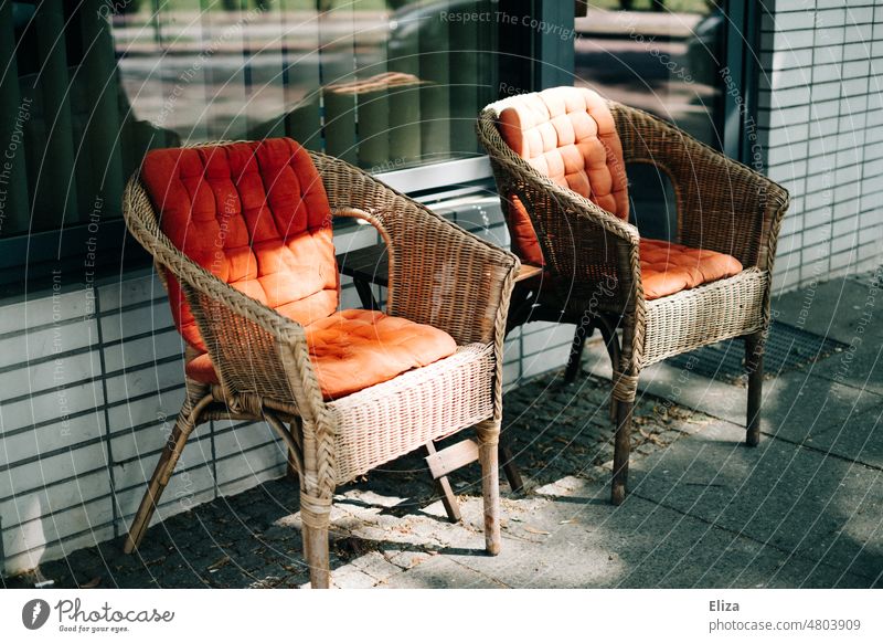 [hansa BER 2022] Two wicker chairs with red seat cushions enjoy the sun's rays in front of a store basket chair Sunbeam two Red Empty Seating Furniture Armchair