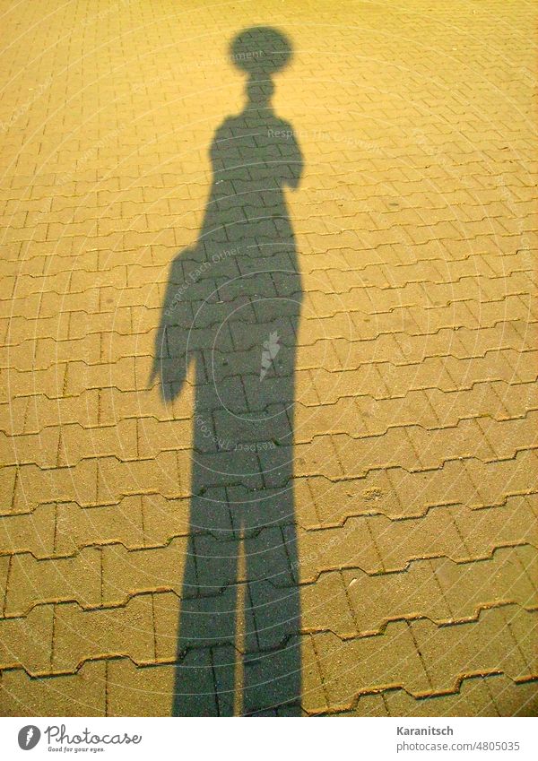 There is a silhouette from a lamp and a person. Shadow light lantern street morning sun self portrait