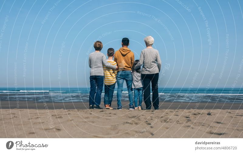 Unrecognizable people in the beach backwards watching the sea unrecognizable group family together child embracing looking outdoors different age ethnic