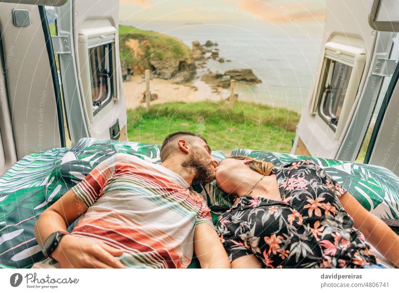 Couple kissing lying on the bed of their camper van young couple landscape trip coast open door sea ocean romantic freedom mobil home smiling enjoy cheerful