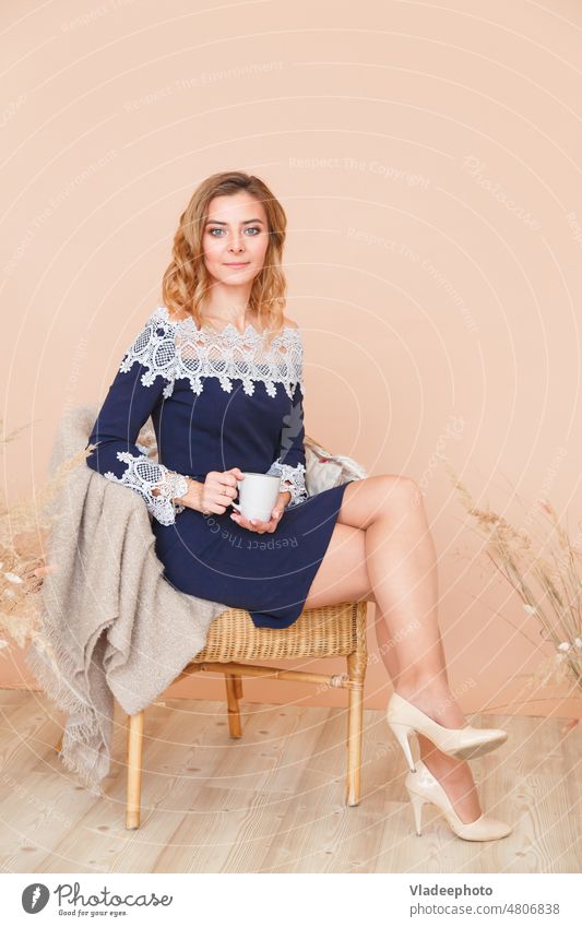 Attractive girl is sitting in a rattan wicker chair with a cup of tea woman armchair indoors coffee jewish lifestyle comfort pastel dead wood house white plaid