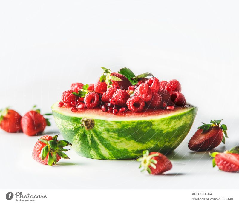 Halved watermelon filled with red summer fruits at white background. halved raspberries strawberries pomegranate seeds delicious healthy sweet dessert