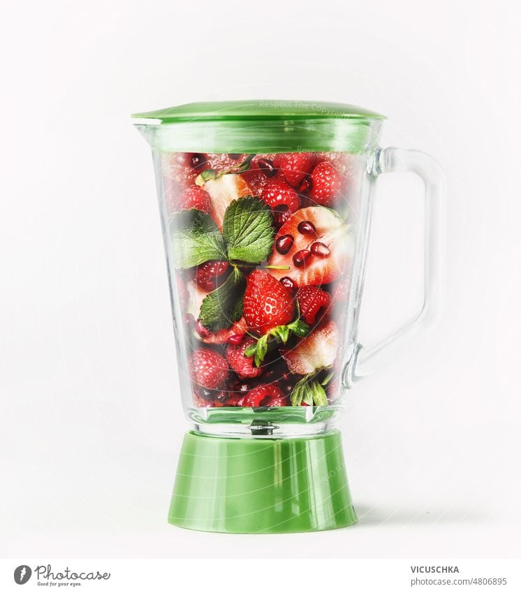 Green blender with red fruits: strawberries, raspberries, mint leaves and pomegranate seeds. smoothie refreshing preparation healthy ingredients front view