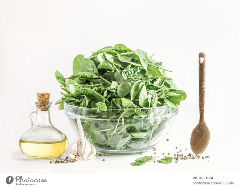 Cooking setting with green spinach leaves in glass bowl, olive oil and wooden spoon at white background cooking healthy food food preparation front view organic