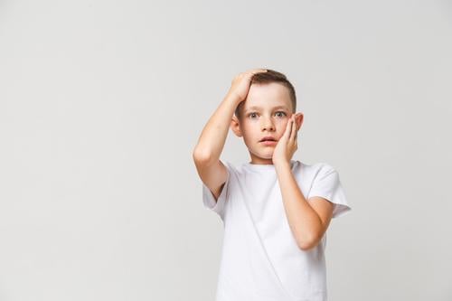 Terrified boy in white t-shirt with both hands on head on gray background horrified terrified scared kid child afraid fear person young emotion expression male