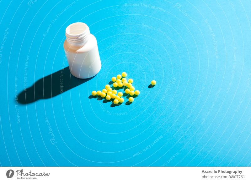 Round yellow ball pills and a plastic bottle on blue background. antibiotic business capsule care chemistry clinic close up concept container covid 19 cure