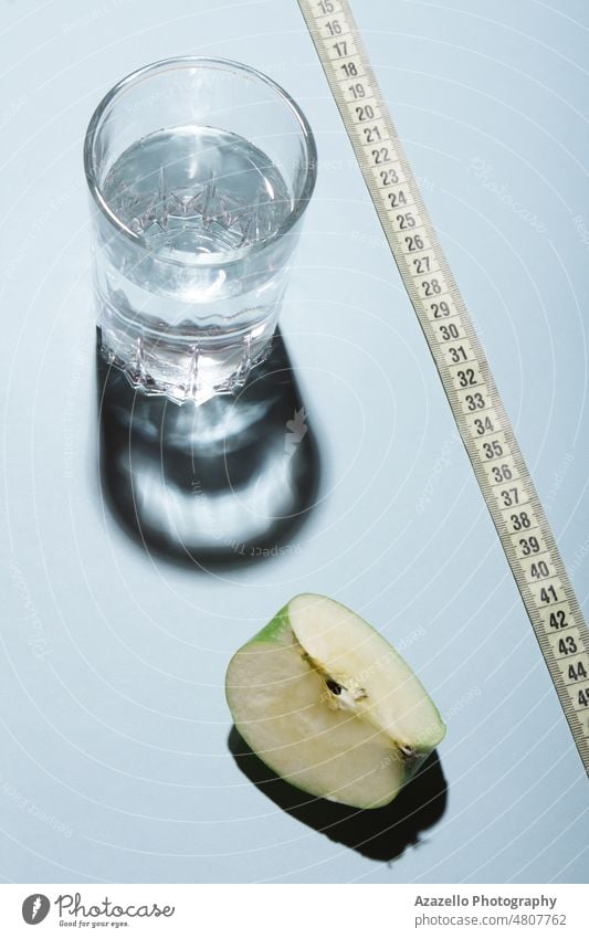 Healthy livestyle diet concept layout. Glass of water with apple slice and a tape measure on blue background. aqua beverage body care clean cold water