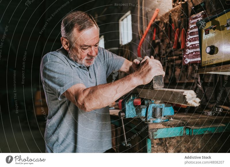 Aged carpenter using plane and working in garage man plank wooden workshop woodwork carpentry tool jointer male joinery craftsman timber lumber workbench