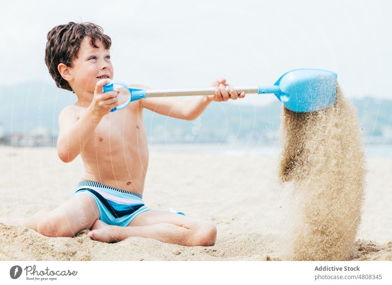 Glad little boy digging sand on beach summer vacation smile shovel weekend glad child coast relax shore kneel childhood rest resort happy kid holiday cheerful