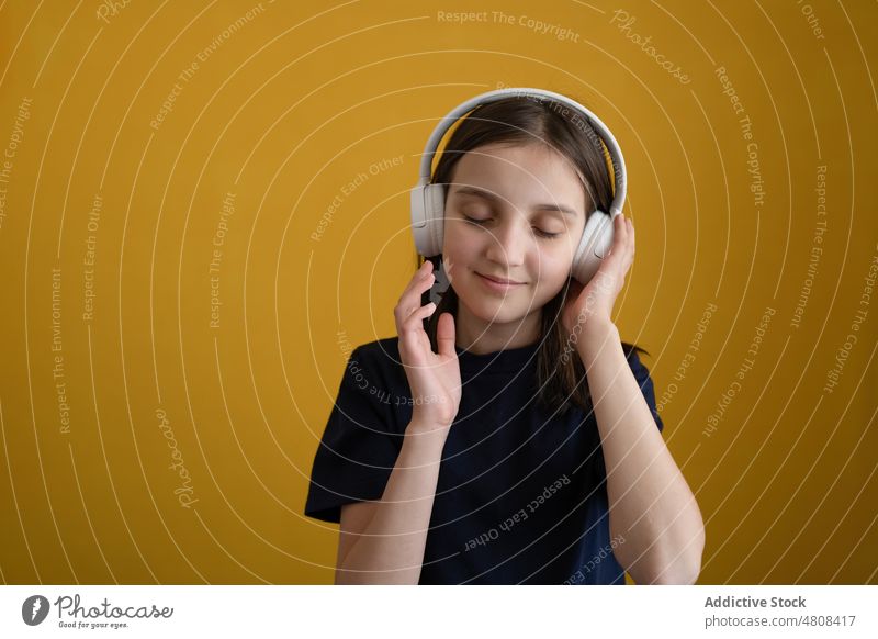 Content kid with closed eyes listening to music in headphones girl eyes closed enjoy song delight sound portrait meloman smile happy preteen brunette casual