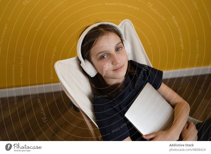 Tranquil girl sitting on chair and listening to song music relax chill enjoy headphones calm meloman melody preteen brunette casual laptop home kid sound rest