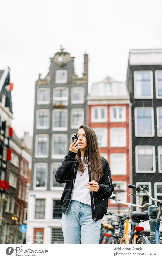 Young lady recording audio message on smartphone in city historic district woman voice communicate street using female young ethnic hispanic amsterdam
