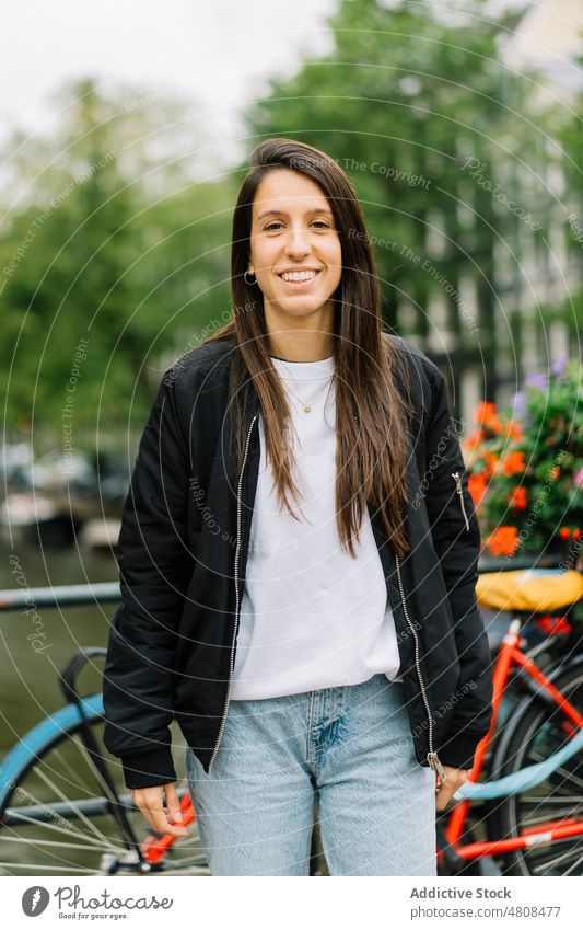 Happy ethnic woman smiling while standing on footbridge on cloudy day smile city canal bicycle traveler happy style holiday trip vacation female young hispanic