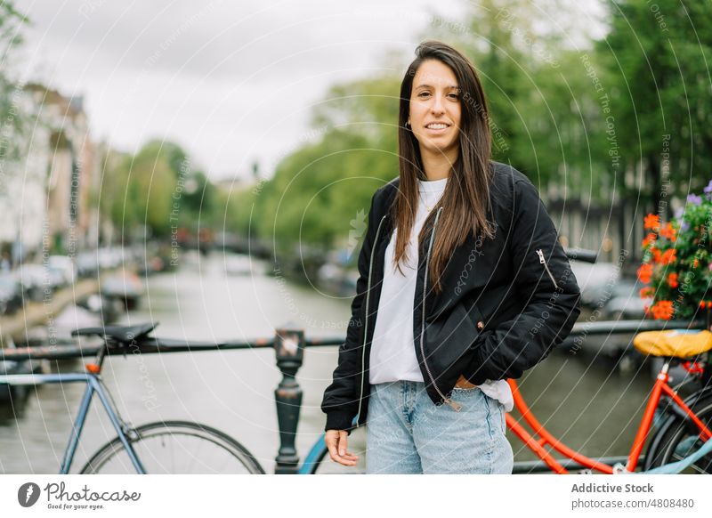 Happy ethnic woman smiling while standing on footbridge on cloudy day smile city canal bicycle traveler happy style holiday trip vacation female young hispanic