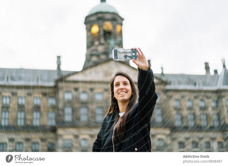 Content ethnic travelling woman taking selfie against historic palace smartphone smile sightseeing traveler building self portrait architecture explore exterior