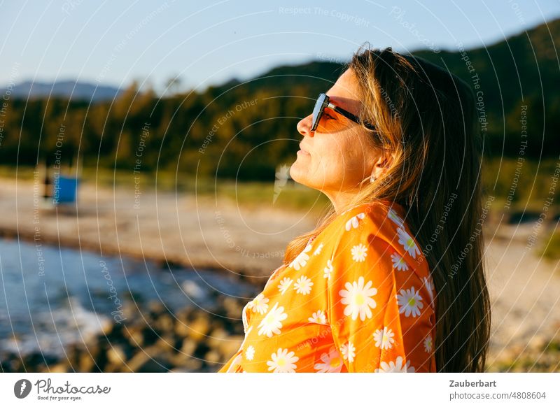 Woman in orange dress with white flowers sits on beach and looks at sunset Dress Orange Beach Sunset Sunglasses vacation Green Landscape Italy Vacation & Travel