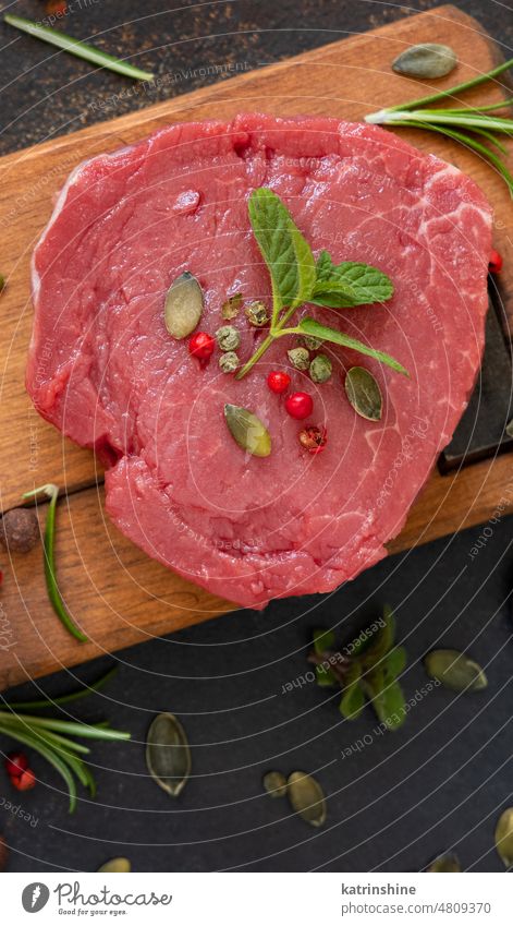 Raw beef fillet steak with herbs and spices on wooden board on dark table top view meat food raw red fresh mignons uncooked nuts green copy space rosemary mint