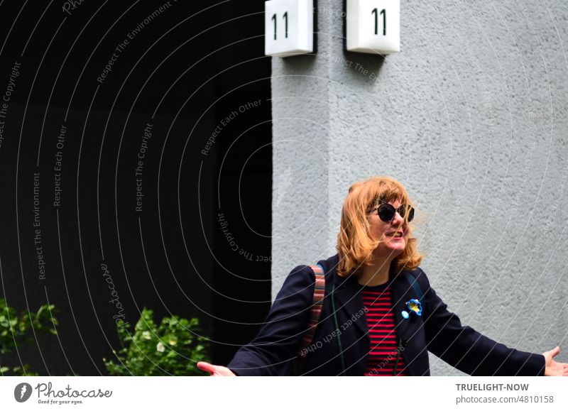 [Hansa BER 2022] Striking entrance to high-rise building no. 11, in front of it a joyfully excited woman with long, reddish-blond hair, huge sunglasses, invitingly wide-spread arms, black-red striped shirt under black jacket