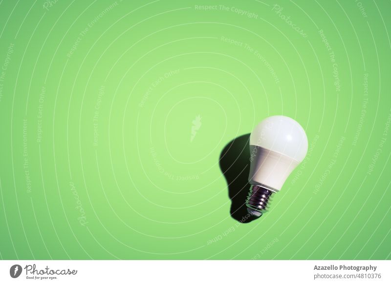White lightbulb on green background under the bright light with black shadow. light bulb electric economy white minimalism still life simple creative color