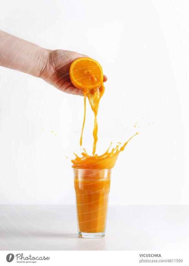 Women hand squeezing orange with splashing juice in glass at white background. women orange juice preparation healthy drink front view bright beverage citrus