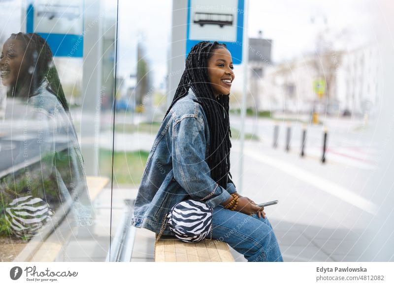 Young woman waiting for a bus at a bus stop cool carefree confident day millennials dreadlocks enjoy authentic positive real people joyful toothy smile