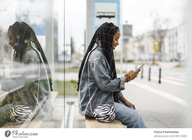 Young woman waiting for a bus at a bus stop cool carefree confident day millennials dreadlocks enjoy authentic positive real people joyful toothy smile