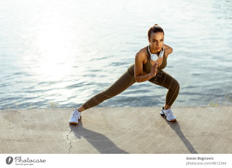 Young woman in sportswear stretching on a river promenade active athletic beautiful caucasian energy exercise female fit fitness flexibility healthy jogger