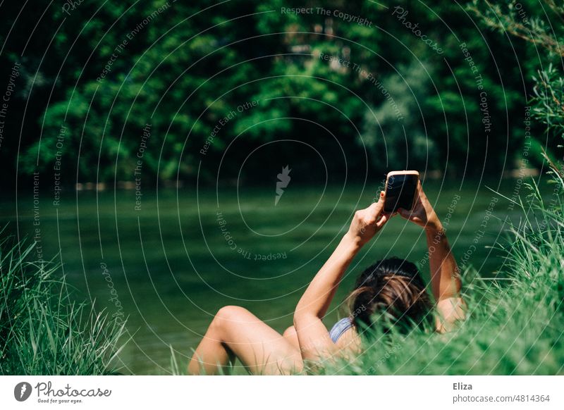 Woman lying in the sun in the greenery by the lake/river and busy with her cell phone Cellphone Lake Nature in the country River Bikini sunbathe Water Summer