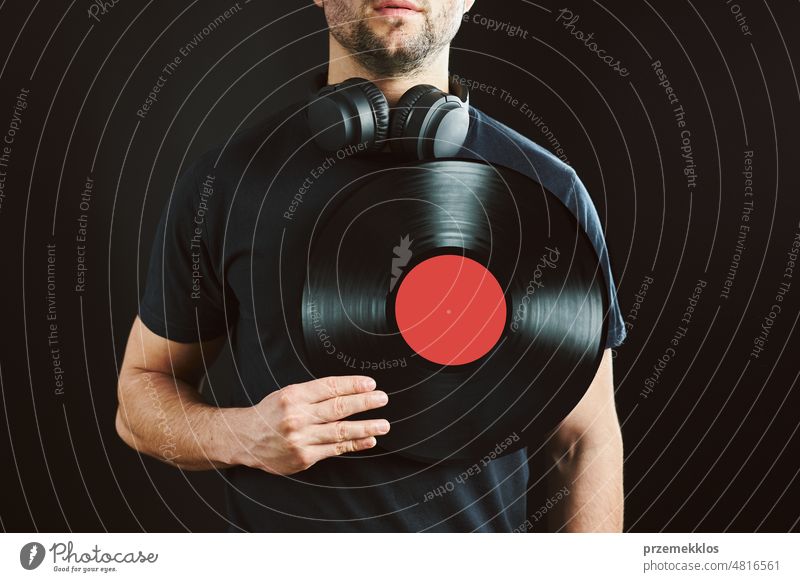Man holding vinyl record over heart. Music passion. Vintage music style. Male with headphones holding old vinyl disk standing on black background. Retro music