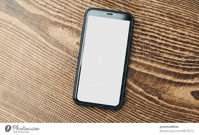 Smartphone mockup with solid white color blank empty isolated screen on wooden background. Black mobile phone top view flat lay with copy space. Room for text