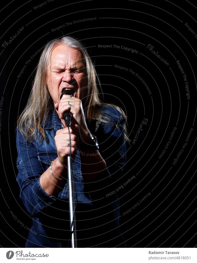 elderly man with long gray hair sings into a microphone long hair song stage black background music old senior male singer happy leisure fun mature concert