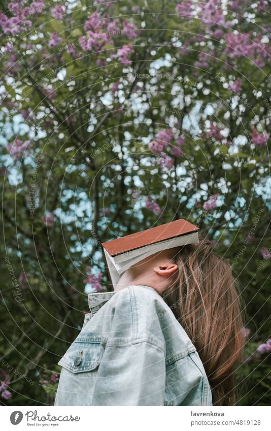Faceless shot of female holding a book in front of her face outdoors people girl person alone denim education faceless green hands intelligent lifestyle park