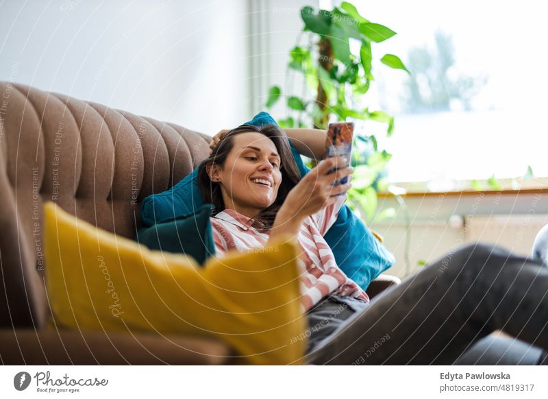Happy young woman using mobile phone on sofa smartphone technology online internet using phone communication domestic life confidence indoors home house people