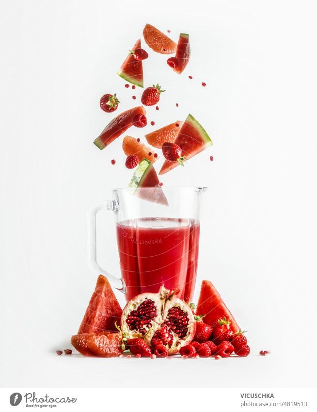 Red smoothie in blender with falling ingredients: grapefruit, watermelon, pomegranate, strawberries and raspberries. healthy refreshing drink vitamins