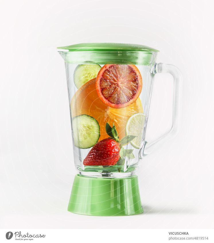Blender with various smoothie ingredients at white background. Healthy refreshing drink preparation blender cucumber orange strawberry lime healthy front view