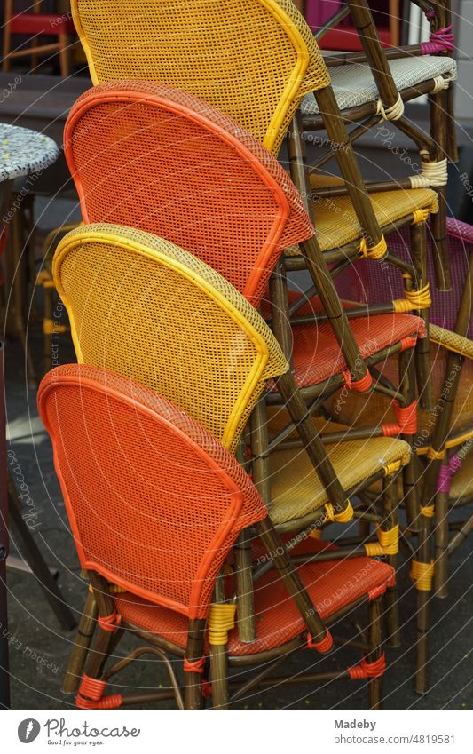 Stacked bistro chairs in yellow and orange in front of a bistro and restaurant on the sidewalk in Berger Straße in the Bornheim district of Frankfurt am Main in Hesse, Germany