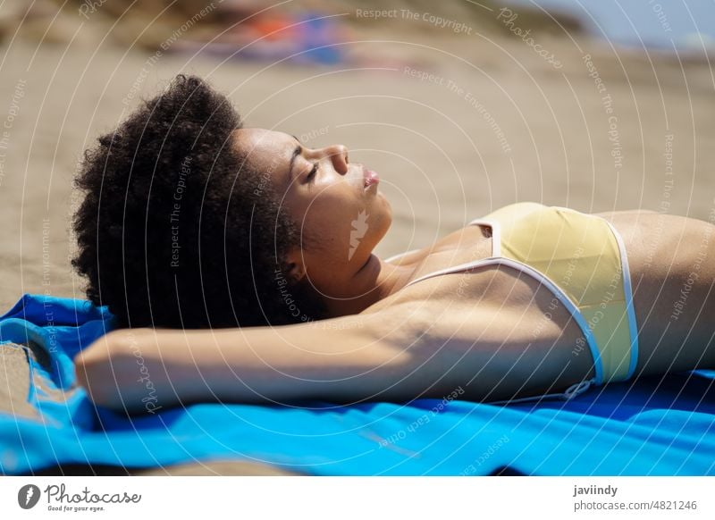 Relaxed black woman lying tanning on the sand of a tropical beach sunbathing. bikini summer swimsuit afro hairstyle relax swimwear coast curly background