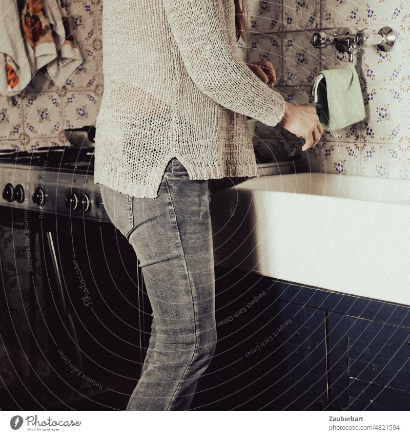 Woman in jeans and white knitted sweater at sink of simple kitchen with gas stove and colorful tiles Kitchen Gas stove Sink Stove Tap Knitted sweater