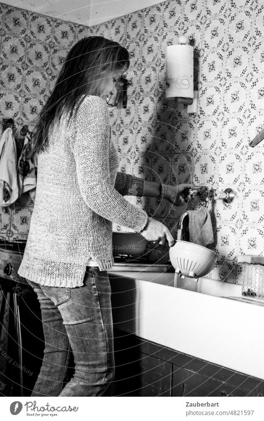 Beautiful woman in sweater and jeans is standing in a simple kitchen at the sink washing up a bowl Woman Long-haired pretty Sweater Kitchen Sink Simple Italian