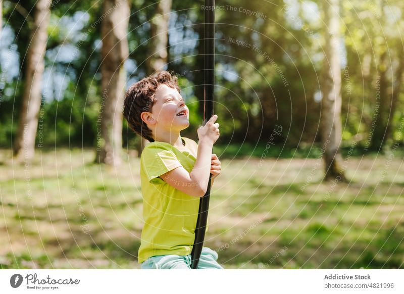 Cheerful little kid on swing rope on playground smiling away child smile childhood cheerful activity boy park positive portrait hang excited joy summer casual