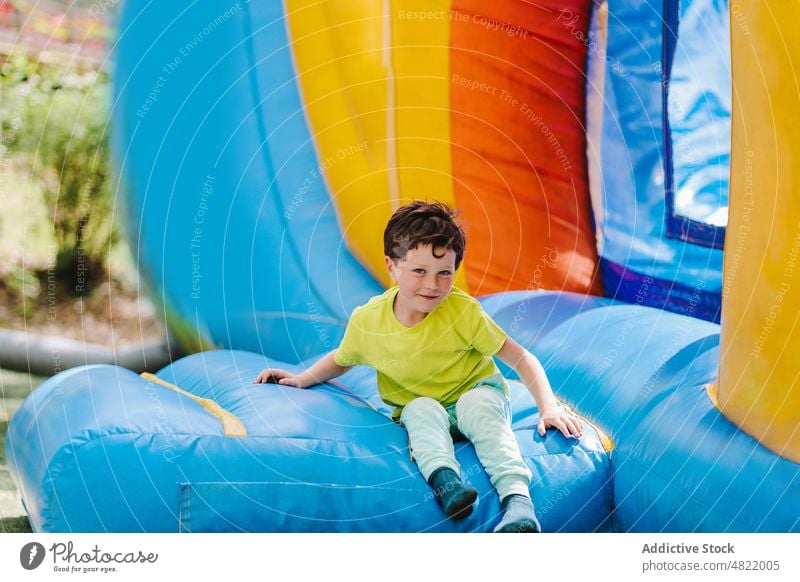Delighted little boy sitting on inflatable trampoline and smiling smile playground castle positive joy child amusement portrait park childhood innocent sunlight