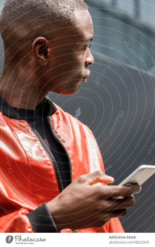 Focused black man using smartphone while leaning on wall on street message city trendy style serious generation z sms communicate chat modern male young
